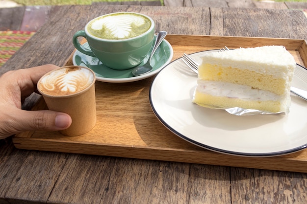 Coconut cake and hot matcha green tea latte and coffee on wooden table.