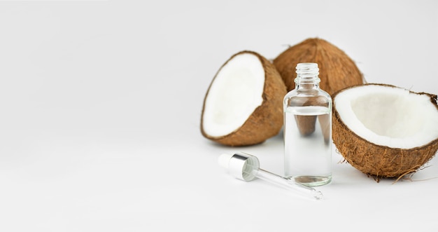 Coconut oil in a bottle with coconuts on a white table. Skin care concept. Face cosmetics.  Copy space.