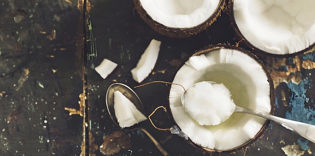 Photo coconut oil in a bowl with a spoon surrounded by fresh coconut halves on a rustic table