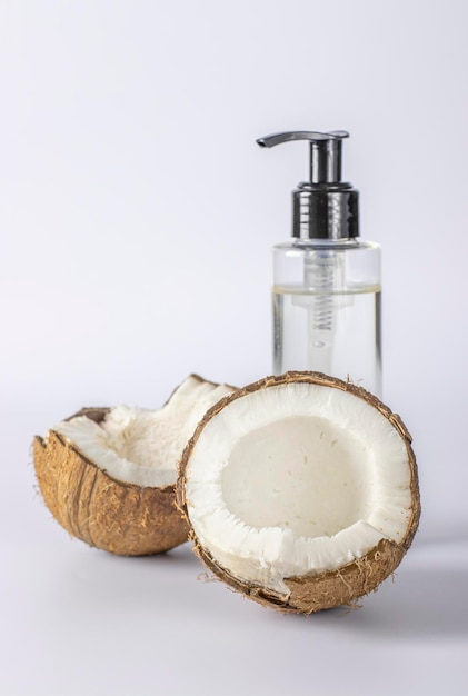 Coconut oil in a transparent bottle and fresh coconut on white background Natural cosmetic product