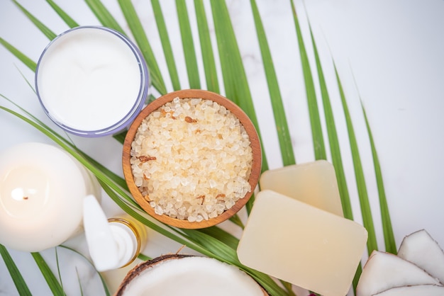 Coconut oil, tropical leaves and fresh coconuts. Spa coconut products on light wooden surface.