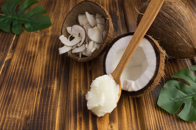 Coconut oil in the wooden spoon and coconut crisps on the brown wooden table. Natural products.