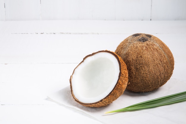 Coconut with half and leaves on white wood table