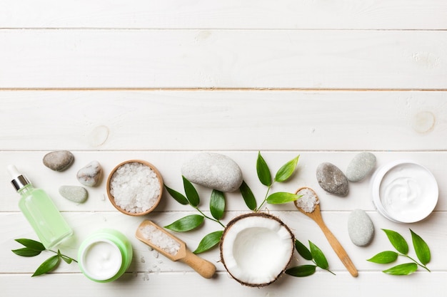 Coconut with jars of coconut oil and cosmetic cream on colored background Top view Free space for your text Natural spa coconut cosmetics and organic treatment concept Coconut Spa composition