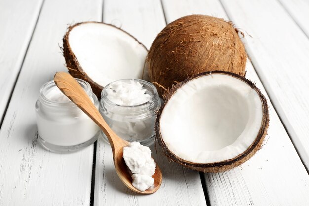 Coconut with jars of coconut oil and cosmetic cream on wooden background