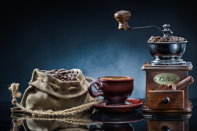 Coffe mill cup and sack with beans on mirror table