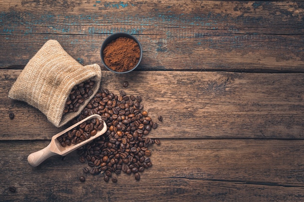 Coffee beans in a bag and ground coffee in a cup on a wooden table with space to copy. Top view, copy space.