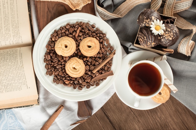 Coffee beans and biscuits on a saucer with a cup of tea