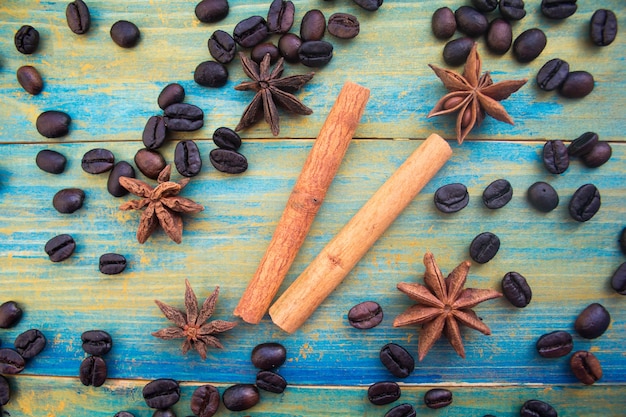 Coffee beans, cinnamon sticks and star anise on wooden background painted in blue and gold. close-up.