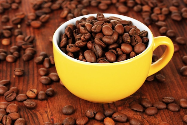 Coffee beans in cup on wooden background