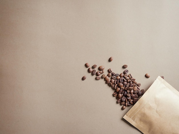 Coffee beans emerging from a paper bag on a plain brown background top view with copy space