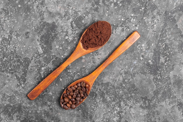 Coffee beans and ground coffee in wooden eco spoons on gray background