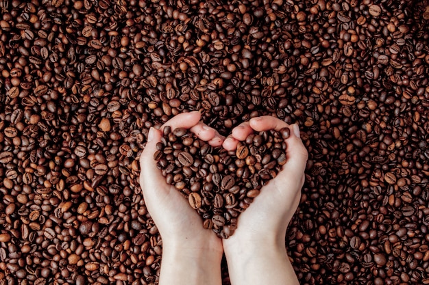 Coffee beans in man palms in form of a heart on coffee background