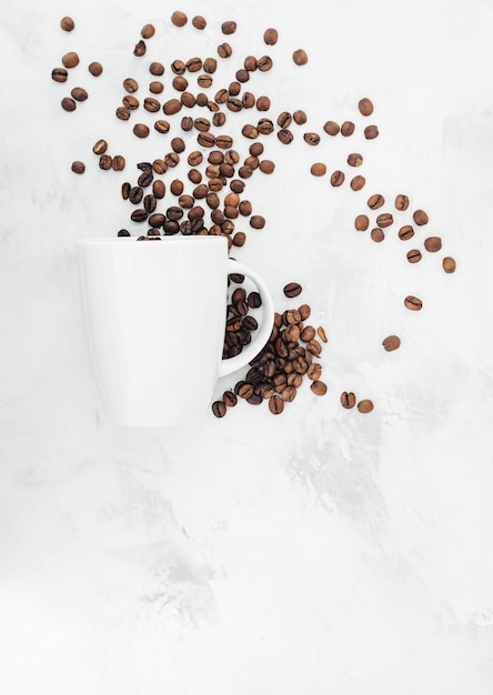 Coffee beans poured out of a cup pile of coffee beans on textured background