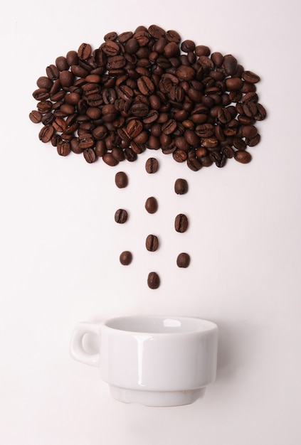 Coffee beans in shape of cloud pouring rain in a white cup on white background. Weather symbol