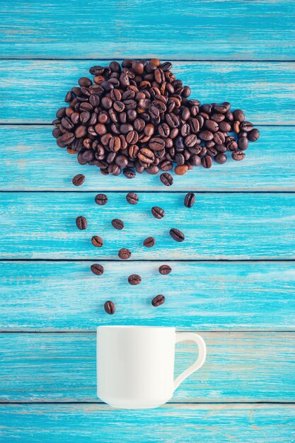 Photo coffee beans in shape of rainy cloud with cup on blue background. weather concept