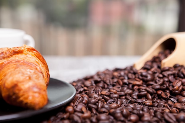 Coffee beans, sweet donut and a cup of coffee in close up photo