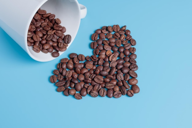 Coffee beans in a white cup Coffee beans are scattered in the shape of a heart on a turquoise