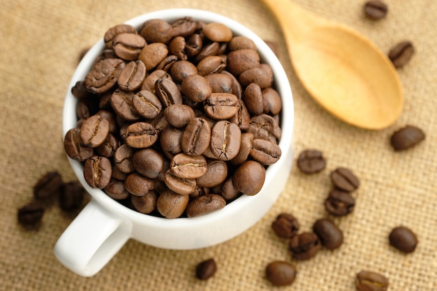 Coffee beans in the white cup placed on sackcloth.