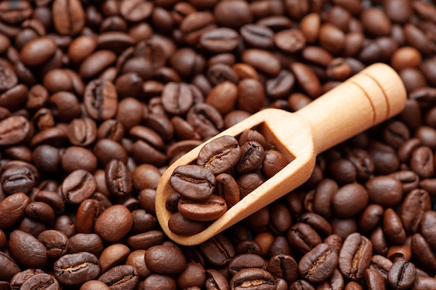 Coffee beans on a wooden scoop against the background of roasted coffee beans