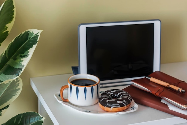 Coffee break in the home office coffee and a donut with chocolate icing on the office desk with notebooks tablet and stationery