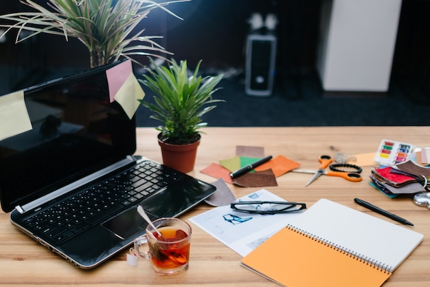 Coffee break. time to reboot and relax. cup of tea standing on the work desk in a comfortable modern office with stationery and supplies scattered