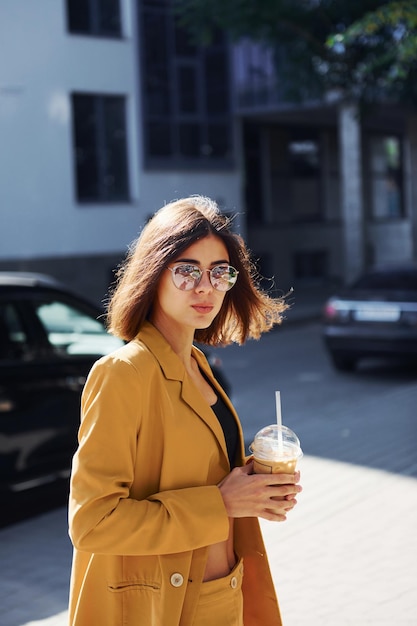 Coffee break Young fashionable woman in burgundy colored coat at daytime with her car