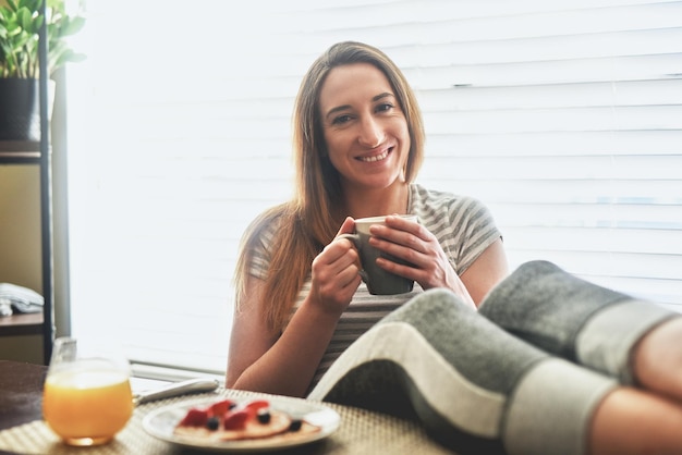 Coffee and breakfast in the morning is what Im about Cropped shot of a young woman having breakfast and chilling by the dining table in the morning at home