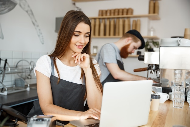 Coffee Business Concept - beautiful caucasian bartender barista or manager working and planing in laptop at modern coffee shop.