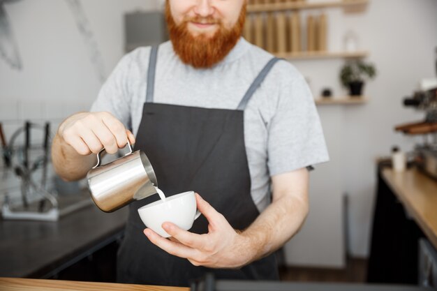 Coffee Business Concept - handsome bearded man in apron making coffee while standing at cafe