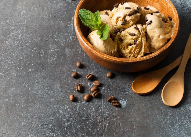 Coffee or chocolate ice cream scoop in wooden plate with mint leaf on dark background