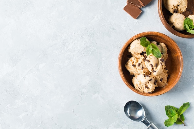 Coffee or chocolate ice cream scoop in wooden plate with mint leaf on light grey background