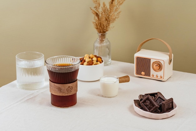 Coffee in a clear glass on the table milk in a milk jug chocolate in a plate