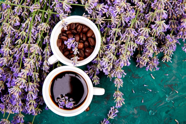 Coffee, coffee grain in cups and lavender flower on green background