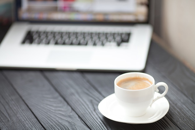 Coffee Cup on the black table on blurred laptop background for Business Concept.