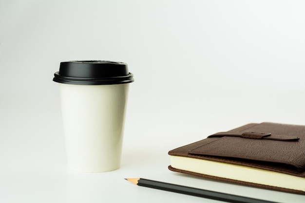 Coffee cup brown and a leather notebook on white desk background with copy space