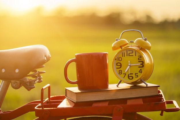 Photo coffee cup, clock, and book put on the red japan style classic bicycle at view of green rice field