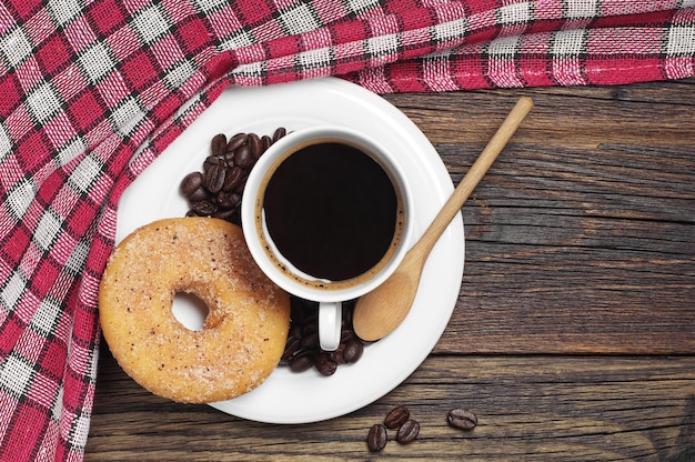 Coffee cup and donut on wooden table with red tablecloth, top view