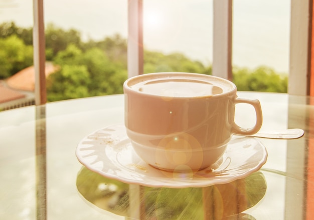 Coffee in a cup on a glass table, a balcony with a view of nature and the sea, a delicious breakfast at sunrise.