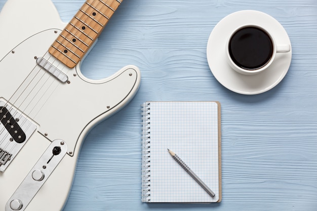 Coffee cup and guitar on wooden table with notebook and pencil