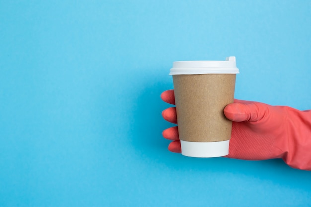 Coffee cup in hand with pink medical gloves isolated on blue background. Female hand with paper cup. Mockup of female hand holding a coffee paper cup. Copy space. coronavirus protection