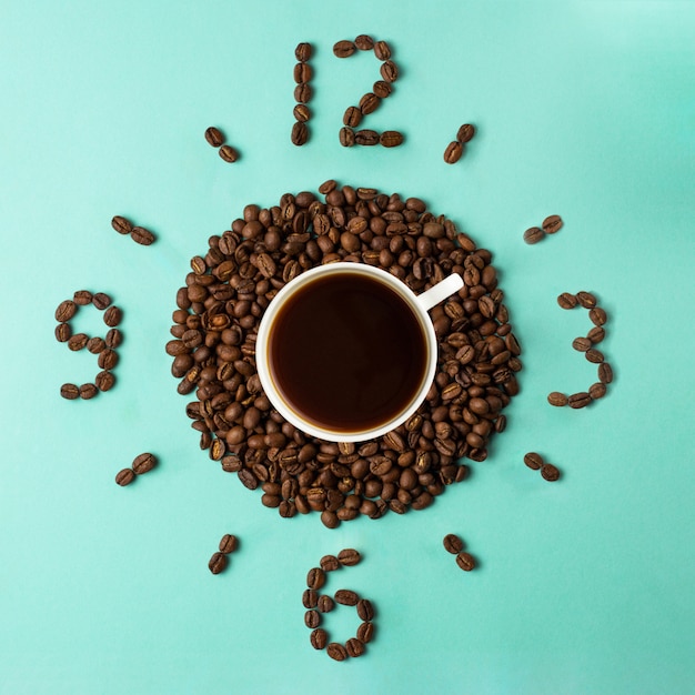 Photo coffee cup and roasted beans arranged as clock face, top view. coffee time. interesting idea energy and refreshment concept.