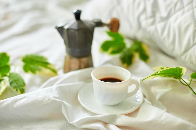 Coffee cup on white bed sheets with geyser coffee maker and green leaves