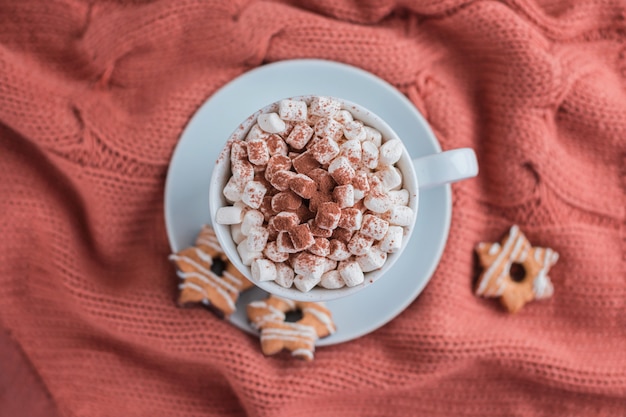 Coffee cup with marshmallow and stars cookies on warm knitted coral blanket.