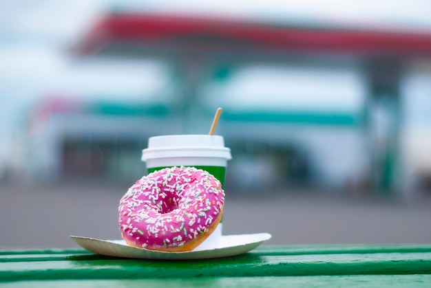 Coffee cup with a pink donut on a background of a gas station.