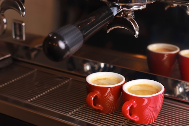 Coffee cups stand inside the coffee machine on a grid, fresh coffee is poured inside the cups