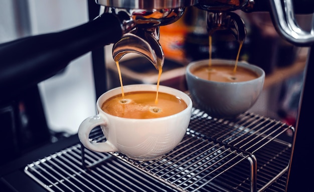 Coffee extraction from the coffee machine with a portafilter pouring coffee into a cup of espresso