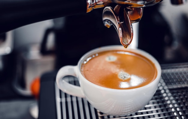 Coffee extraction from the coffee machine with a portafilter pouring coffee into a cup.Espresso