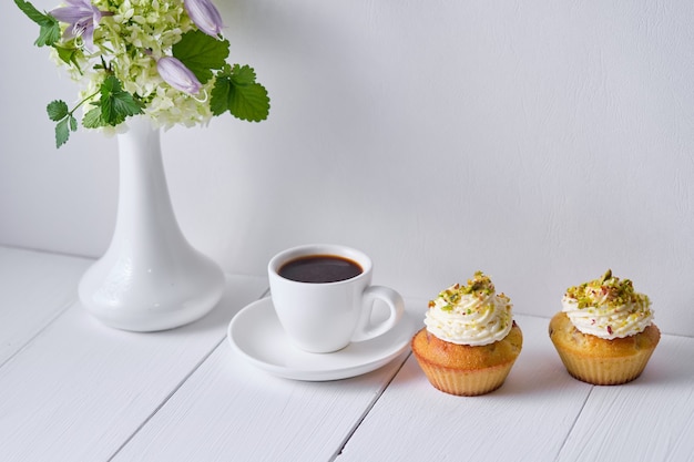 Coffee and fruit cupcakes for breakfast. Morning table with dessert, espresso and flowers in a vase on a white wooden table.