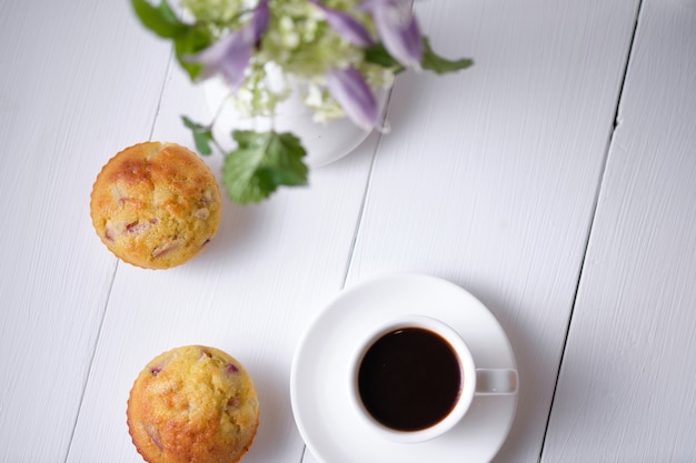 Coffee and fruit muffins with fresh peach for breakfast. Morning table with dessert, espresso and flowers in a vase on a white wooden table. Top view